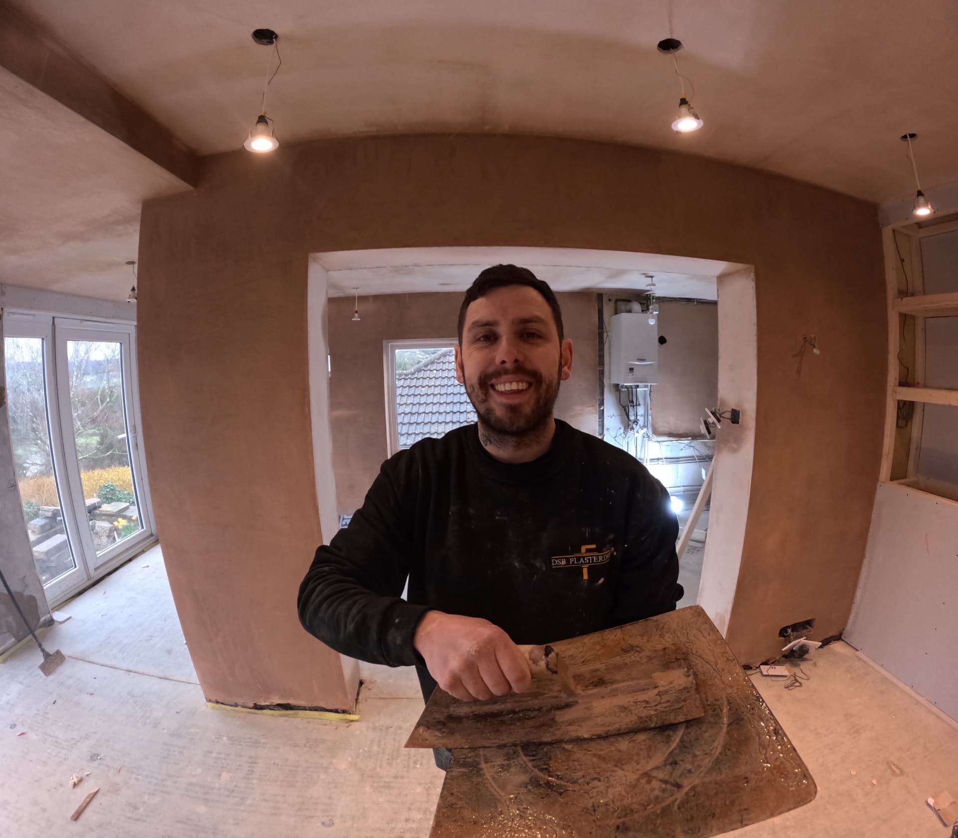 DSB plasterer in branded workwear holding a trowel and hawk in a freshly plastered room